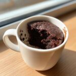 Close-up of a rich chocolate mug cake inside a white mug, with a piece already eaten.