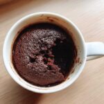 Overhead view of a freshly baked chocolate mug cake in a white mug, with a piece already scooped out.