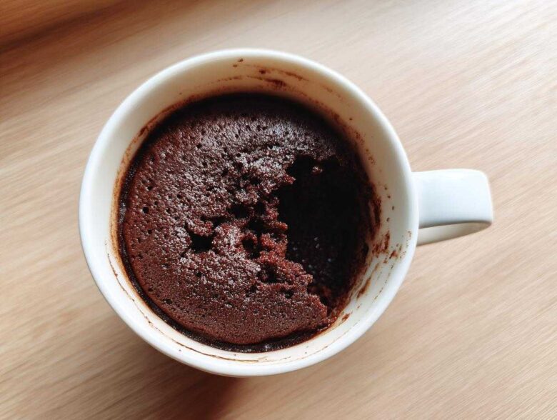 Overhead view of a freshly baked chocolate mug cake in a white mug, with a piece already scooped out.