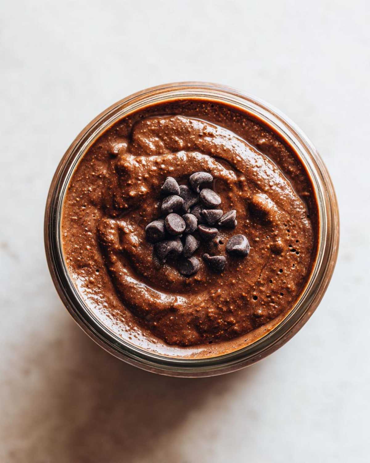 Overhead view of thick chocolate overnight oats in a glass jar, topped with mini chocolate chips.