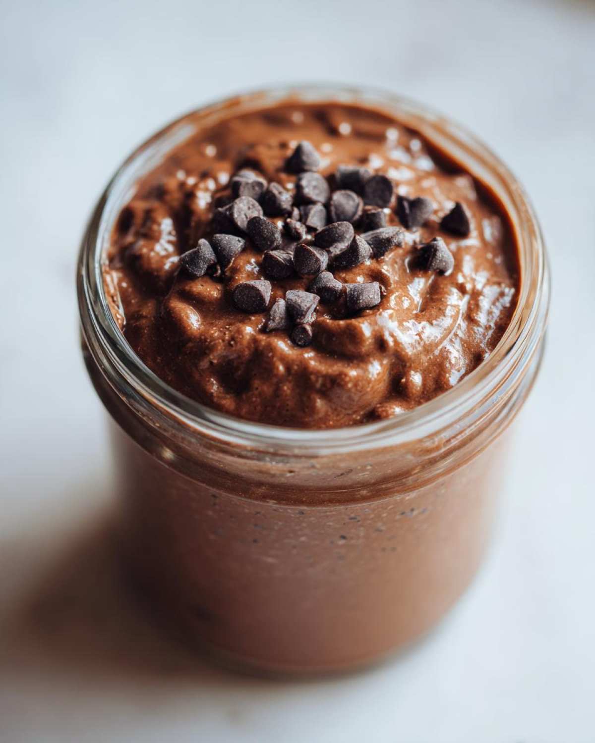 Close-up of rich chocolate overnight oats in a glass jar, topped with dark chocolate chips.