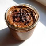 Overhead view of rich chocolate overnight oats topped with mini chocolate chips and cocoa powder in a glass jar.