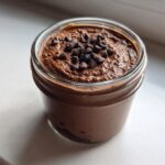 Close-up of creamy chocolate overnight oats topped with mini chocolate chips in a glass jar.