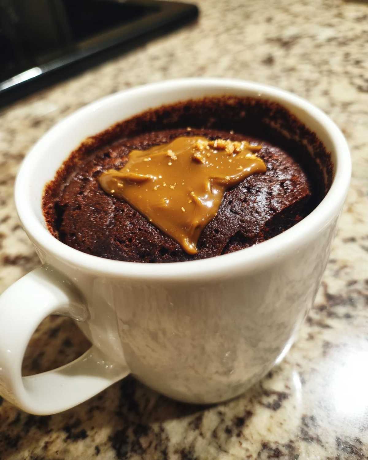 Close-up of a rich chocolate protein mug cake topped with melted caramel sauce.