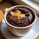 Close-up of a rich, dark chocolate protein mug cake topped with melted peanut butter.