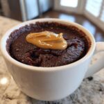 Close-up of a rich chocolate protein mug cake topped with a dollop of peanut butter in a white mug.