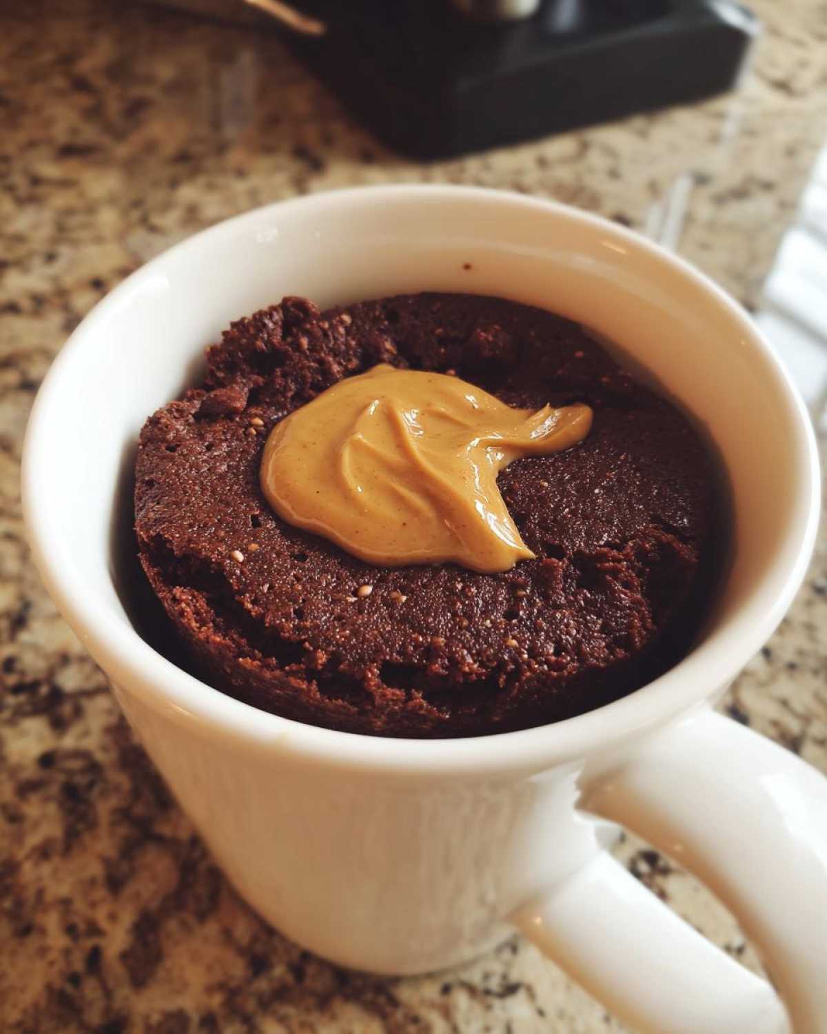 Close-up of a rich, dark chocolate protein mug cake topped with a swirl of creamy peanut butter in a white mug.