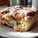 A close-up of a fluffy, glazed piece of cinnamon roll casserole served on a white plate.