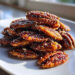A pile of glistening, caramelized cinnamon sugar pecans dusted with visible sugar crystals on a white plate.