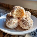 A stack of soft cinnamon sugar snowball cookies on a white plate, one cookie is broken open showing the texture.