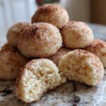 A stack of soft, round cinnamon sugar snowball cookies, with one cookie broken open to show the crumb.