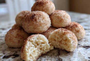 A stack of soft, round cinnamon sugar snowball cookies, with one cookie broken open to show the crumb.