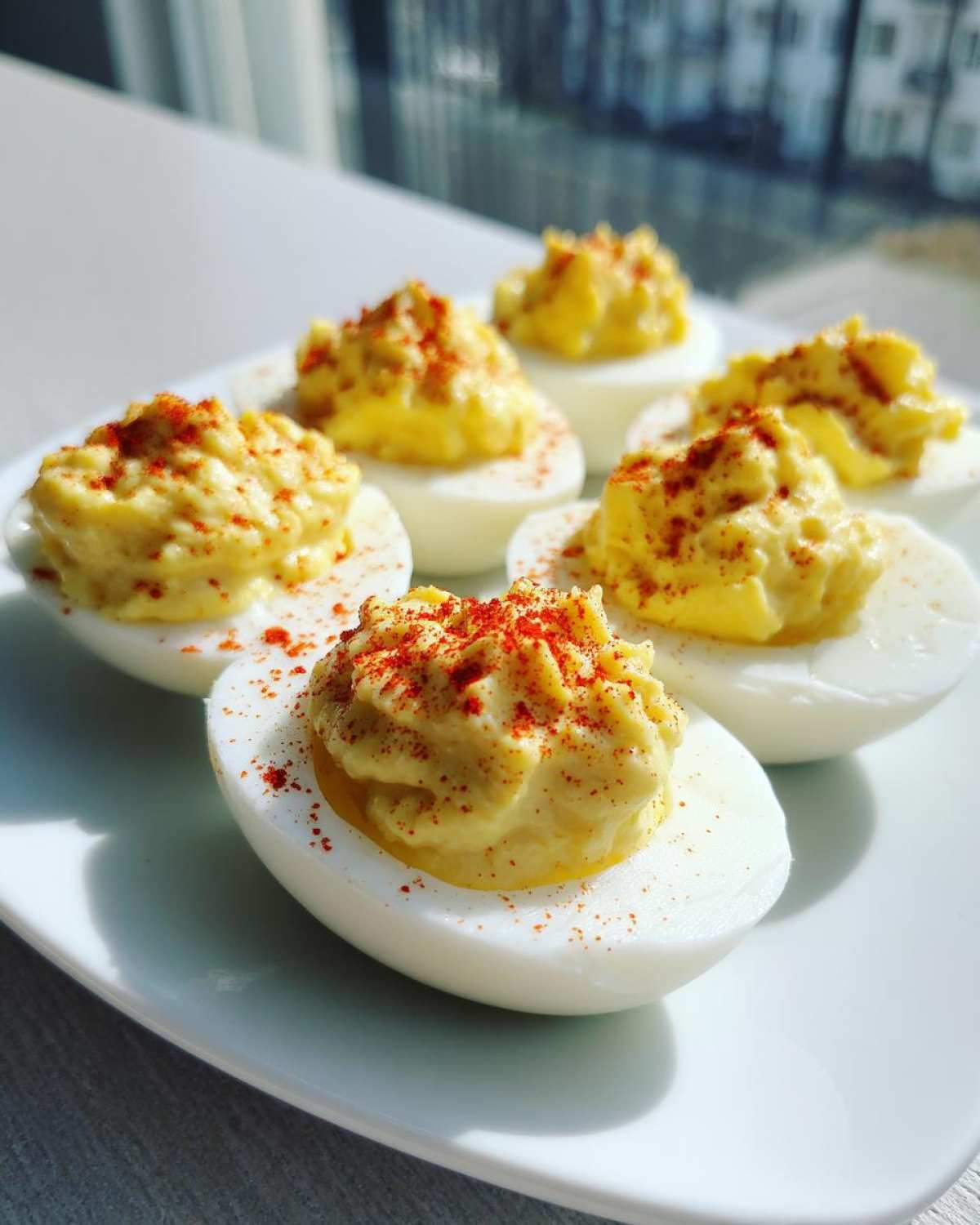 Six creamy deviled eggs, piped high and sprinkled with paprika, served on a white plate.