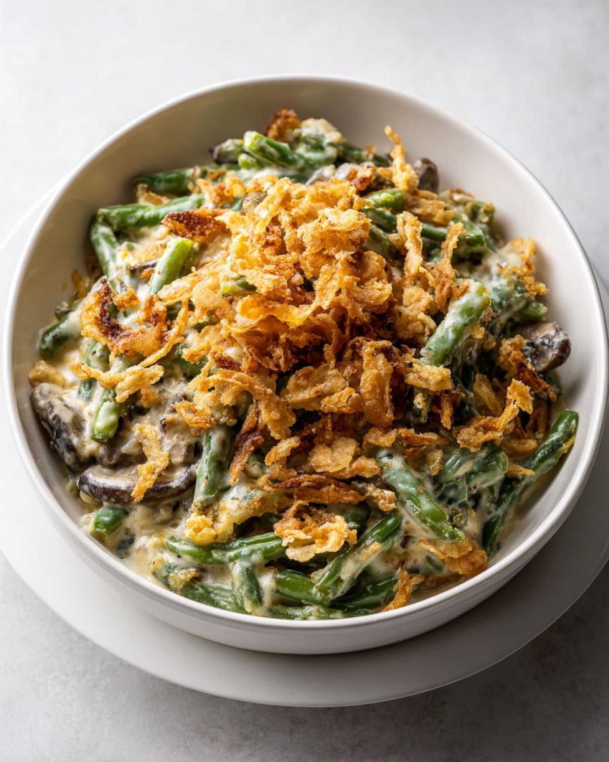 A white bowl filled with creamy green bean casserole topped generously with crispy fried onions.