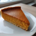 A perfect slice of classic pumpkin pie recipe showing its rich orange filling and crust on a white plate.