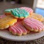 A stack of flower-shaped sugar cookies decorated with bright pink, yellow, and teal cookie icing.