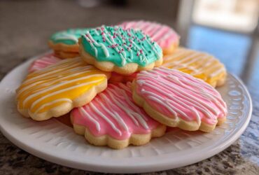 A stack of flower-shaped sugar cookies decorated with bright pink, yellow, and teal cookie icing.