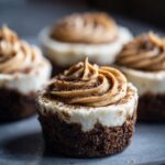 A close-up of one cookie butter cheesecake cup with a dark crust, white filling, and swirled cookie butter frosting.