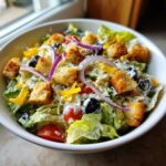 A vibrant bowl of copycat Olive Garden salad featuring crisp lettuce, croutons, cheese, olives, and red onion.