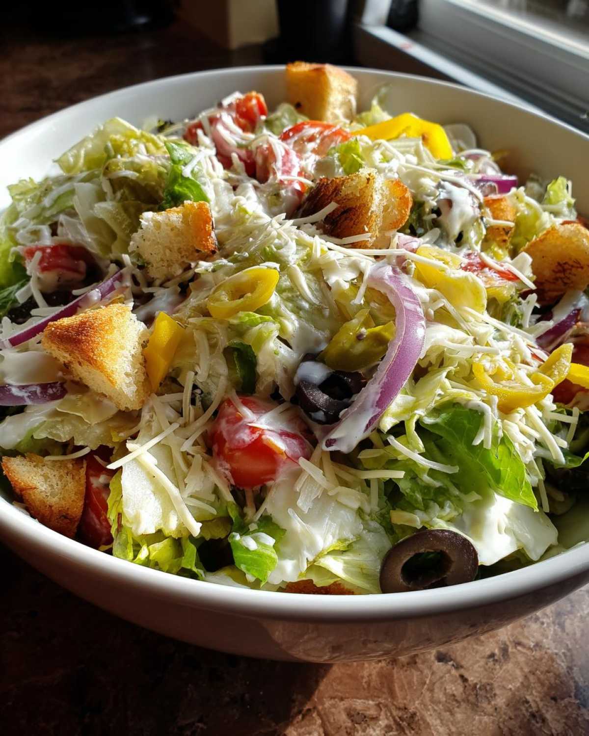 A close-up view of a fresh copycat Olive Garden salad topped with croutons, cheese, red onion, and creamy dressing.