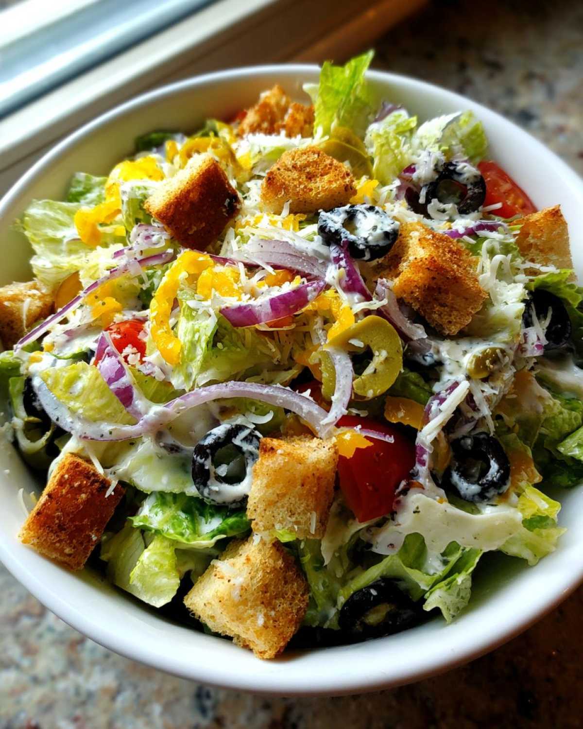 A vibrant bowl of copycat Olive Garden salad featuring crisp lettuce, croutons, black olives, and creamy dressing.