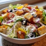 A close-up shot of a fresh copycat Olive Garden salad topped with creamy dressing, croutons, and olives.