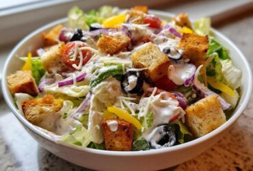 A close-up shot of a fresh copycat Olive Garden salad topped with creamy dressing, croutons, and olives.