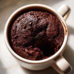 Close-up overhead view of a dark, rich Cottage Cheese Microwave Brownie baked inside a light-colored mug.