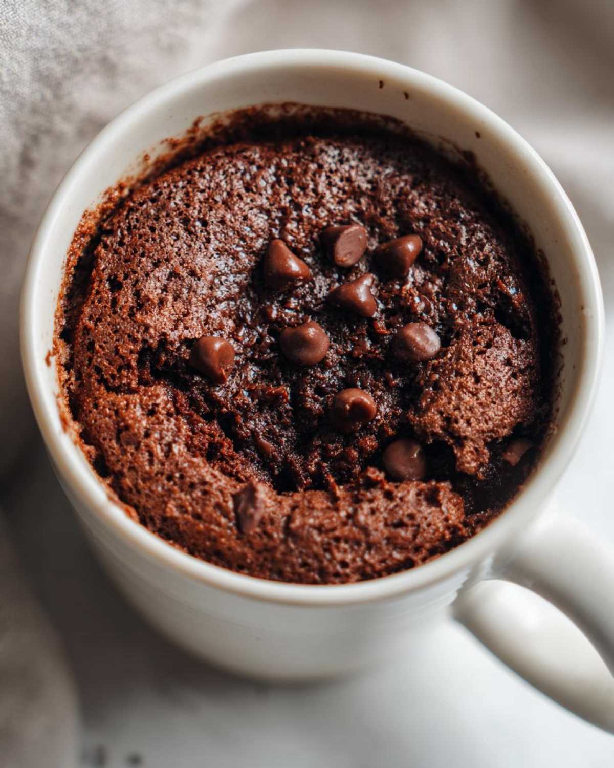 Close-up of a rich, dark chocolate Cottage Cheese Microwave Brownie topped with melted chocolate chips in a white mug.