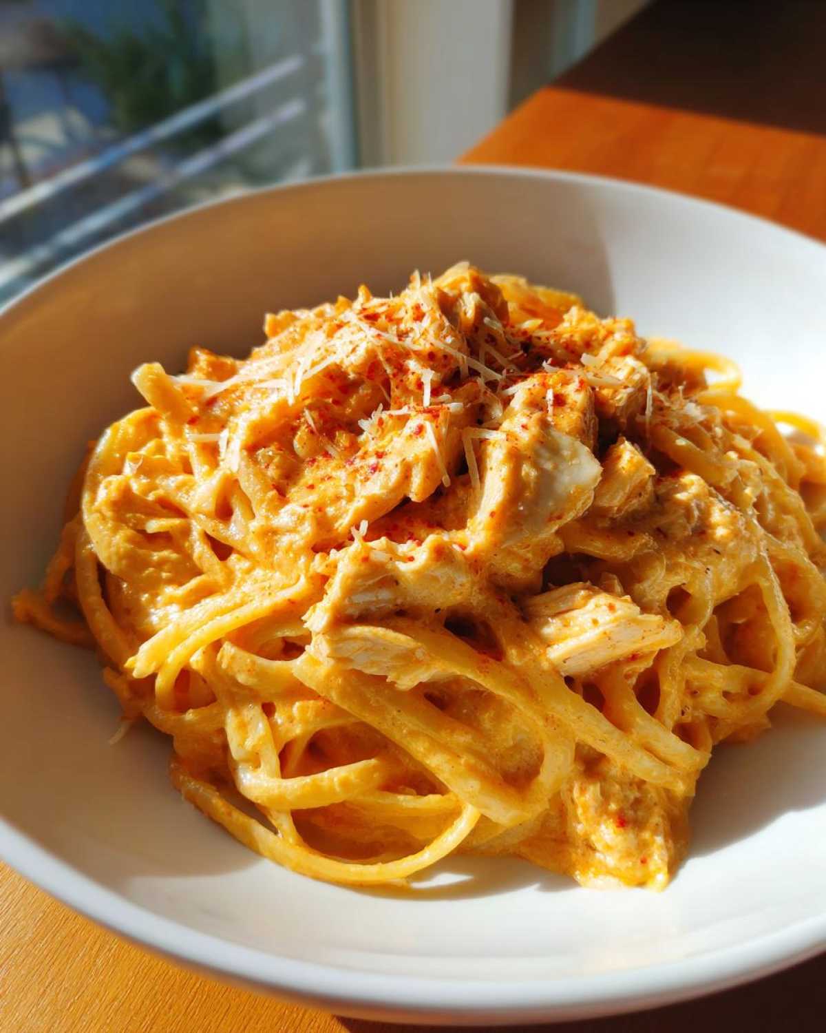 Close-up of creamy, orange-hued cajun pasta topped with shredded cheese and red pepper flakes.