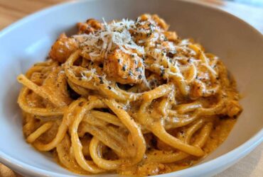 A close-up of creamy Cajun chicken pasta tossed in a rich sauce, topped with grated cheese and herbs.