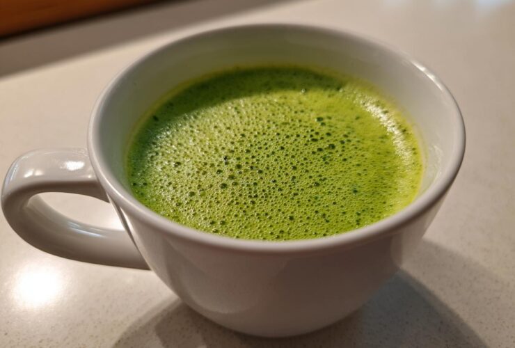 Close-up of bright green, foamy celery soup served hot in a white mug.