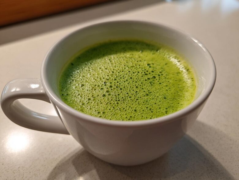 Close-up of bright green, foamy celery soup served hot in a white mug.