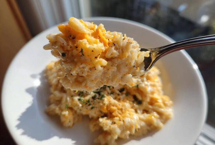 A spoonful of creamy, melted cheesy rice being lifted above a white bowl, showing melted cheddar.