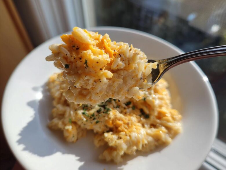 A spoonful of creamy, melted cheesy rice being lifted above a white bowl, showing melted cheddar.