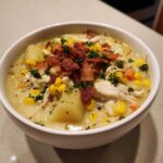 A close-up of a bowl of creamy chicken corn chowder, featuring chunks of chicken, potatoes, corn, and bacon crumbles.