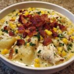 A close-up of creamy chicken corn chowder loaded with chunks of potato, corn, shredded chicken, and topped generously with crispy bacon bits.