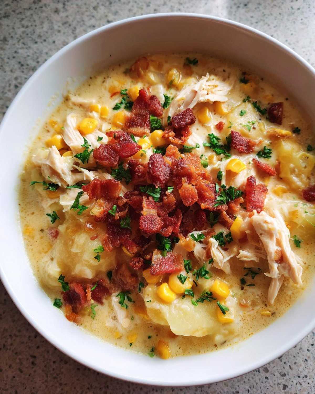 Close-up of a bowl of creamy chicken corn chowder topped generously with shredded chicken, corn, bacon bits, and parsley.