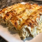 Close-up of three creamy chicken enchiladas covered in bubbly, browned cheese and sprinkled with herbs.