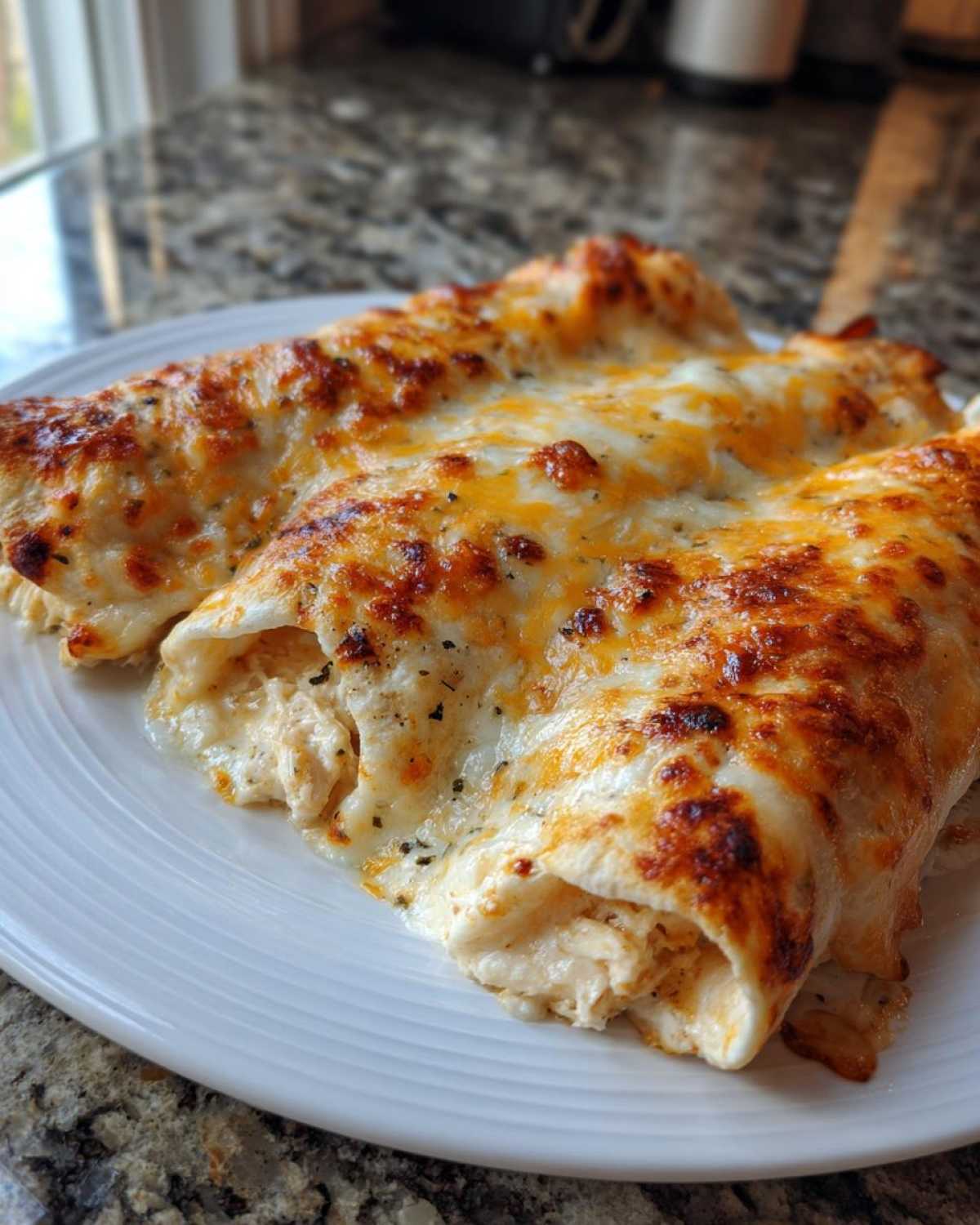Close-up of three creamy chicken enchiladas smothered in melted, browned cheese.