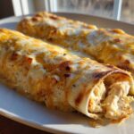 Close-up of two baked chicken enchiladas covered in melted white and yellow cheese, showing shredded chicken filling.
