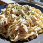 Close-up of creamy chicken fettuccine alfredo pasta garnished with fresh parsley, served on a dark grey plate.