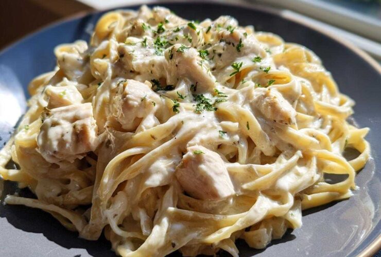 Close-up of creamy chicken fettuccine alfredo pasta garnished with fresh parsley, served on a dark grey plate.