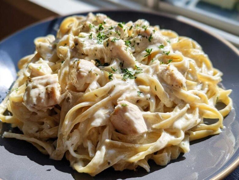 Close-up of creamy chicken fettuccine alfredo pasta garnished with fresh parsley, served on a dark grey plate.