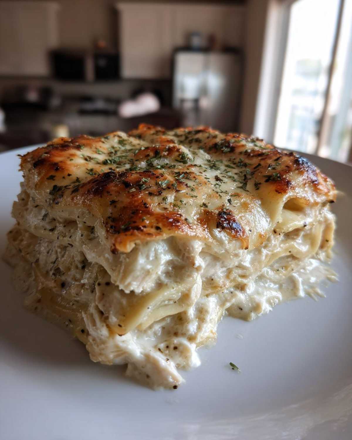 A thick, layered slice of creamy white chicken lasagna with a browned, cheesy top sprinkled with herbs.