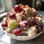 A close-up of creamy chicken salad chick grape salad topped with pecans and cinnamon in a white bowl.