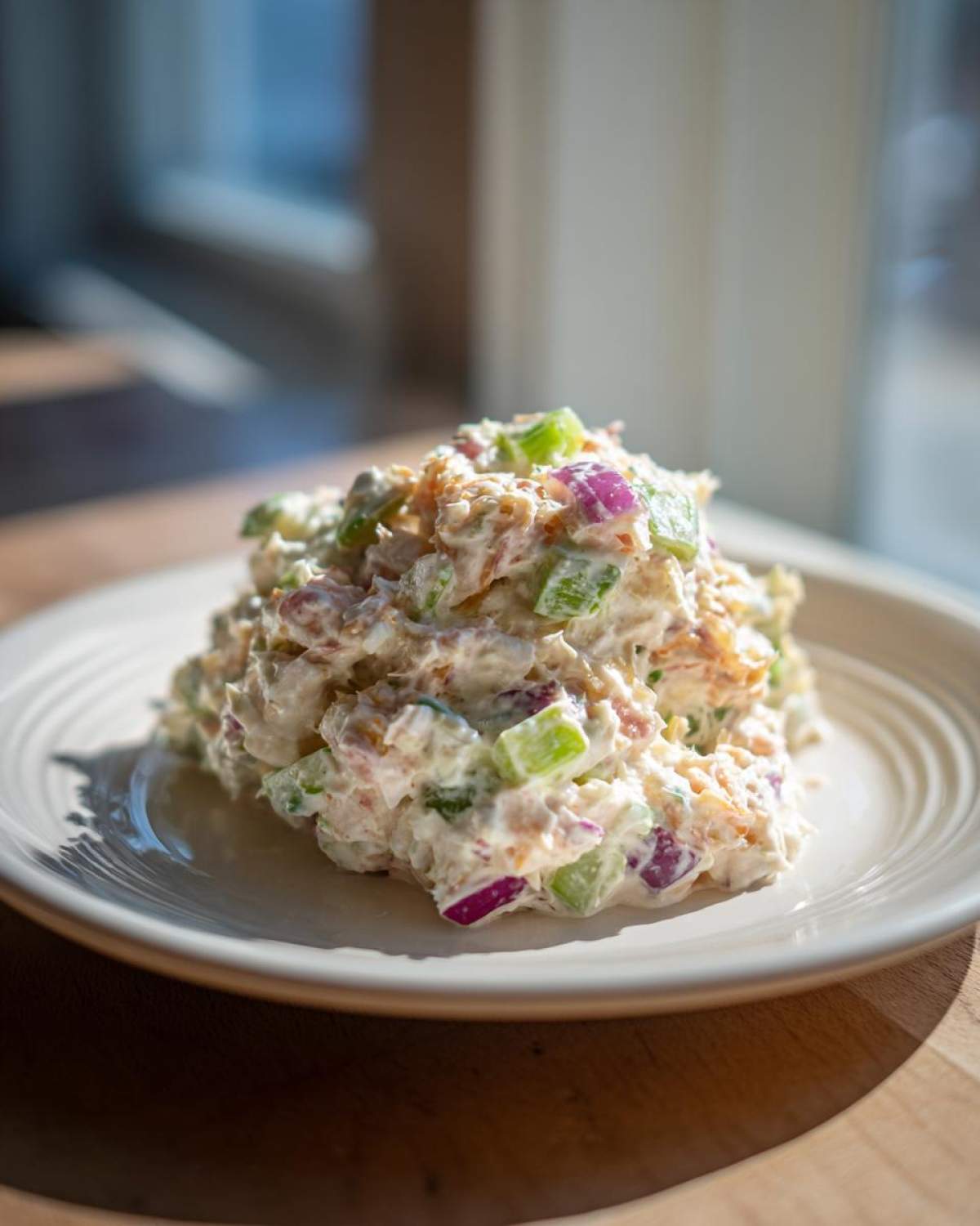 A mound of creamy crab salad featuring visible chunks of celery and red onion served on a white plate.