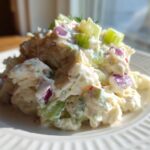 Close-up of a mound of creamy crab salad featuring chunks of celery and red onion on a white plate.