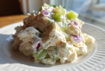 Close-up of a mound of creamy crab salad featuring chunks of celery and red onion on a white plate.
