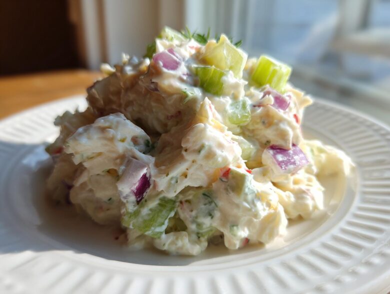 Close-up of a mound of creamy crab salad featuring chunks of celery and red onion on a white plate.